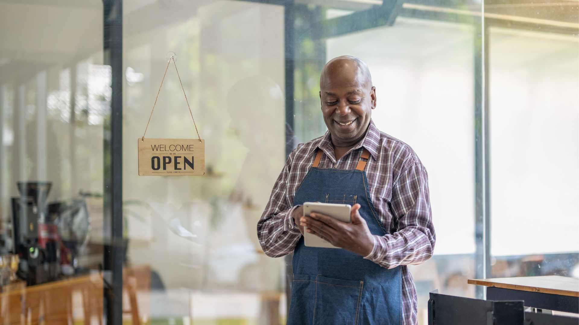 A man is standing in front of a restaurant looking at a tablet.