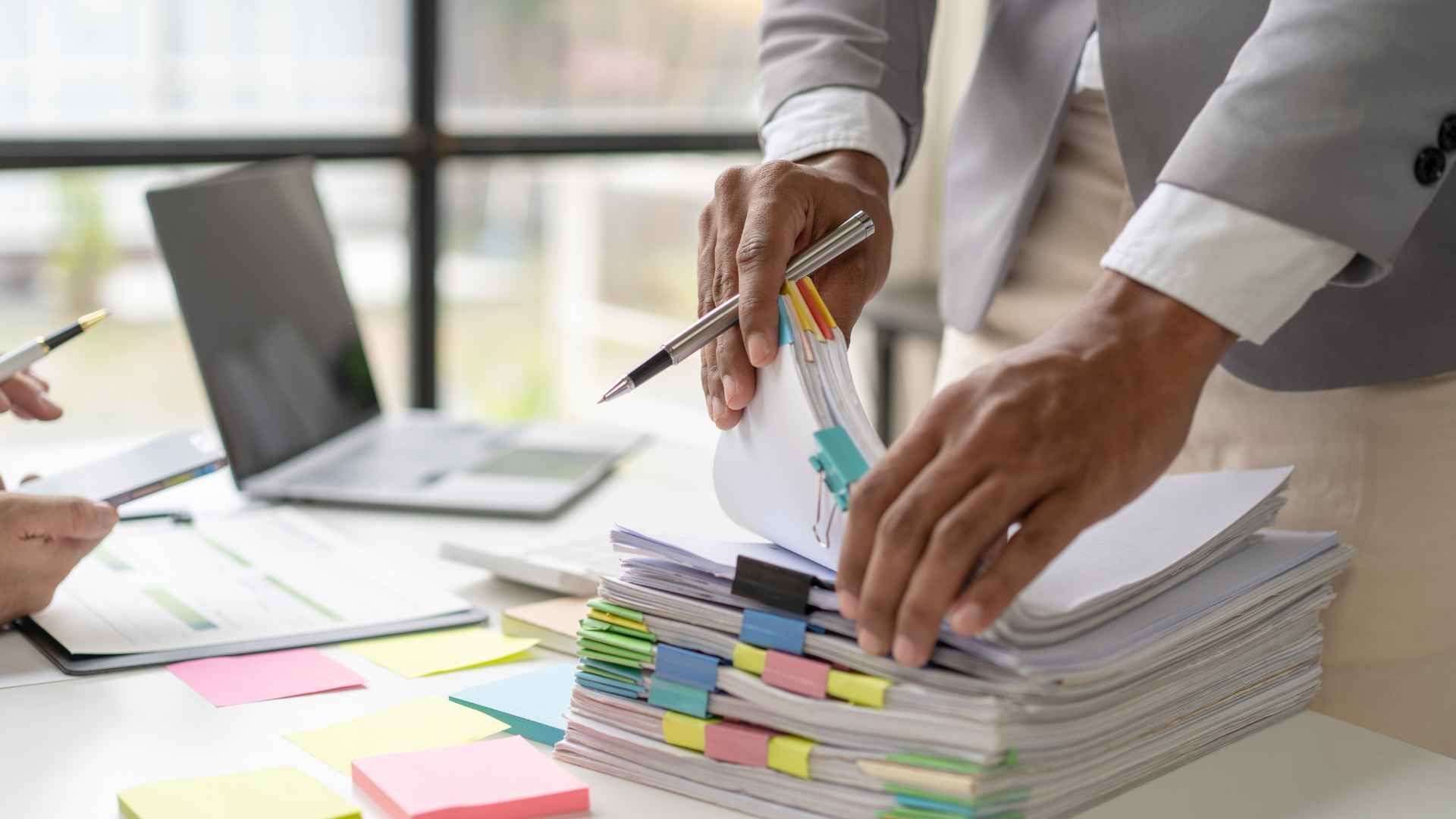 A man is holding a pen over a stack of papers.