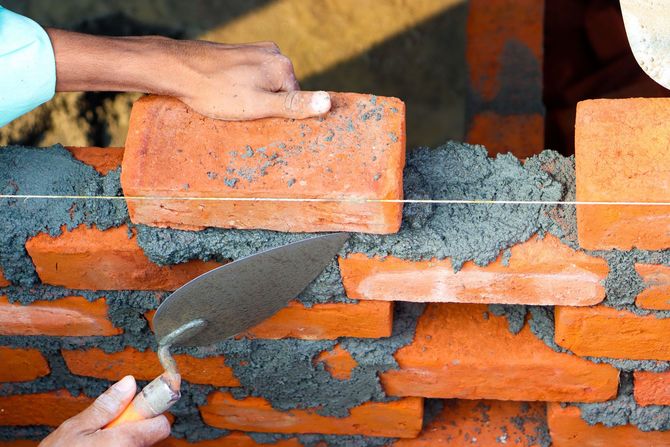 Hands and trowel laying orange bricks with gray mortar on a wall