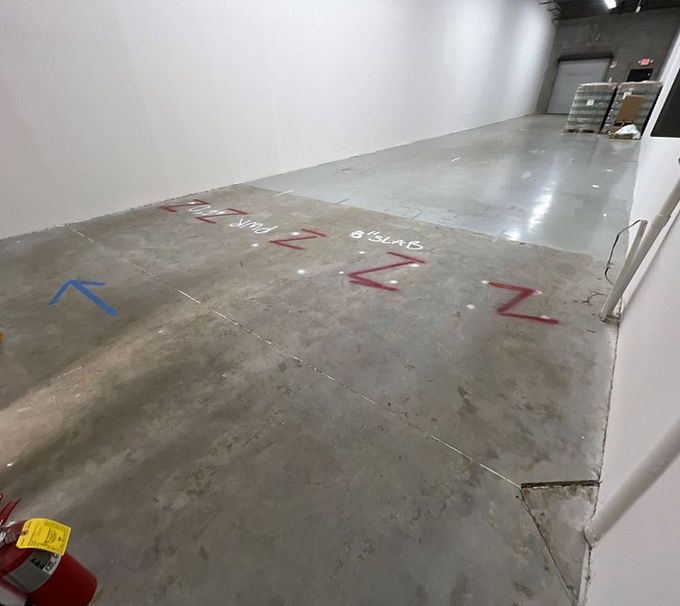 Empty concrete warehouse aisle with red and blue floor markings and stacked items in the distance