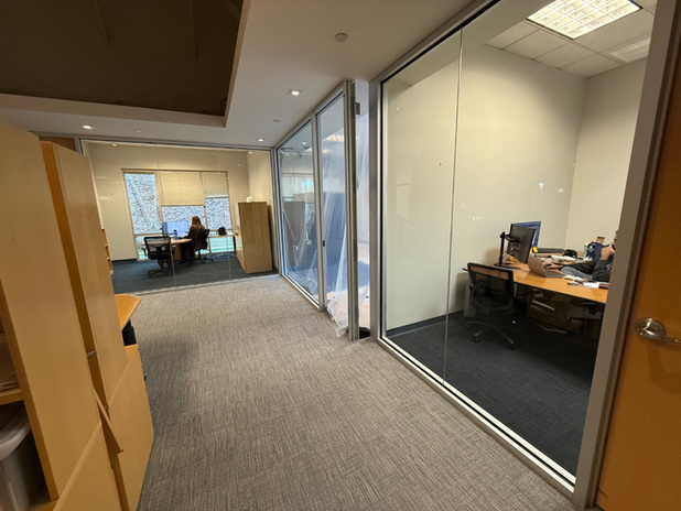 Office hallway with glass-walled meeting rooms and desks visible inside