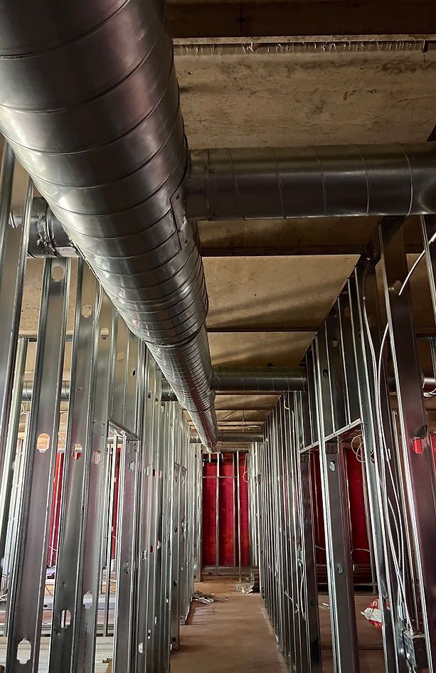 Unfinished hallway with exposed metal framing, ductwork, and red drywall panels under construction
