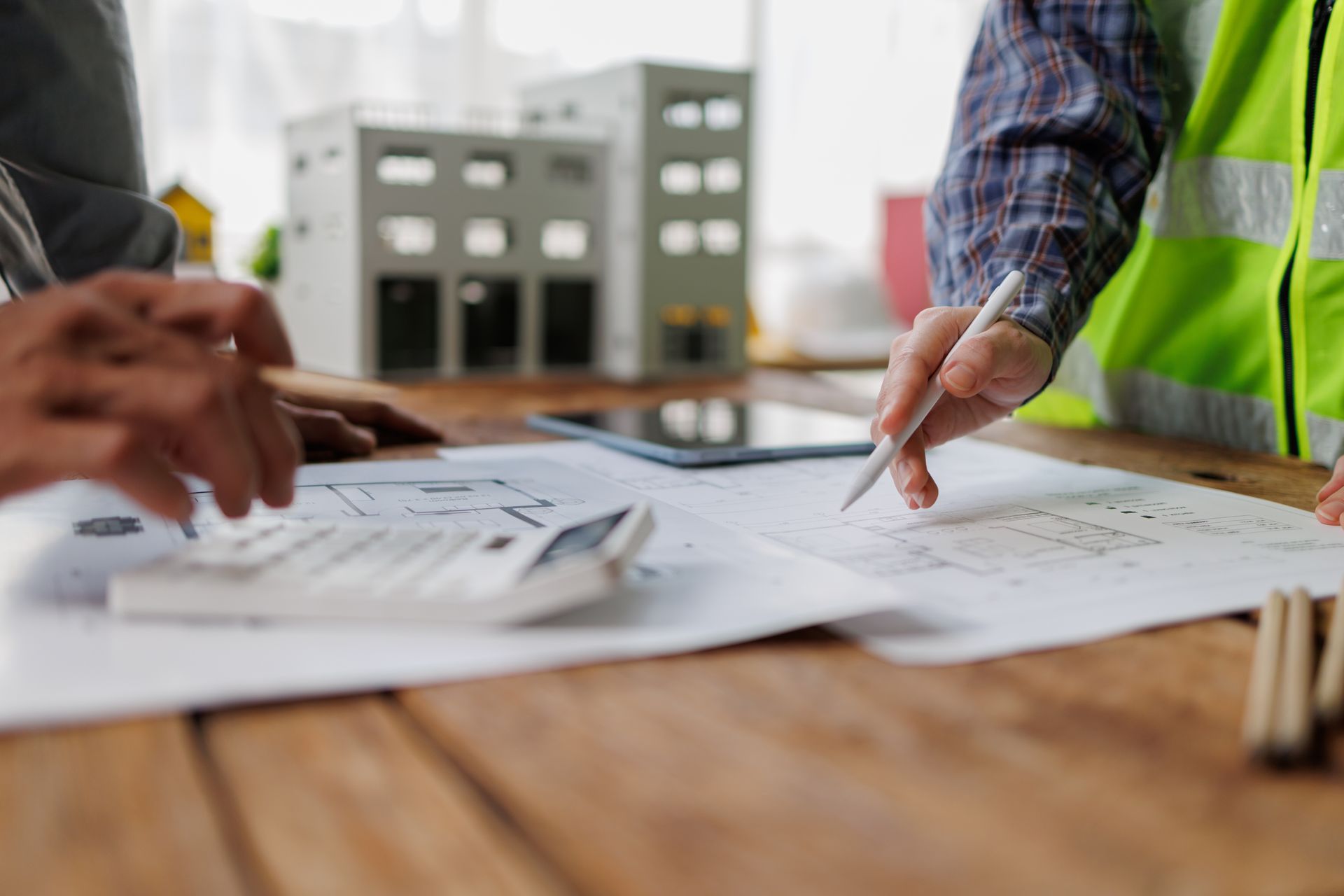 People reviewing construction plans at a table, with a high-visibility vest visible.