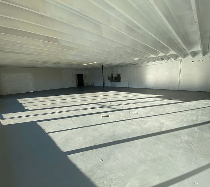 Empty white warehouse with sunlit floor and long diagonal shadows from skylights