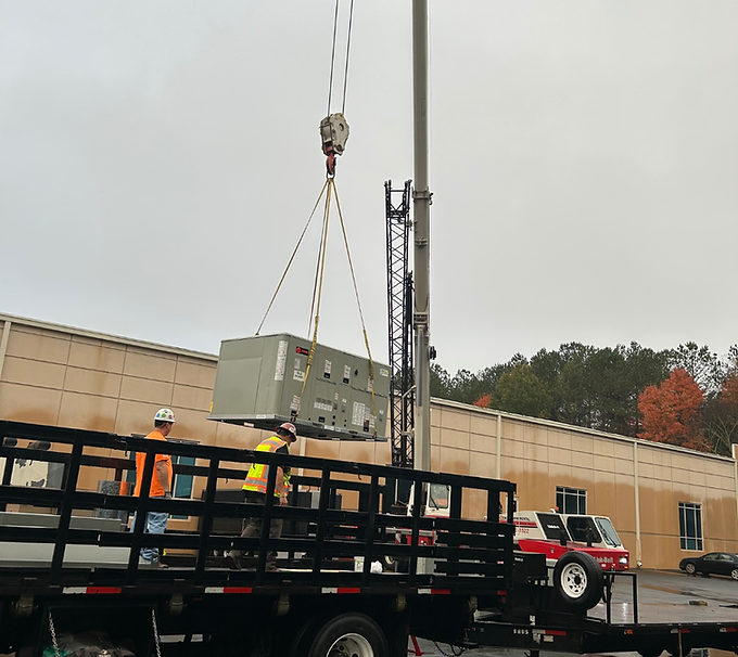 Crane lifts a large gray generator onto a flatbed truck at a construction site in rainy weather
