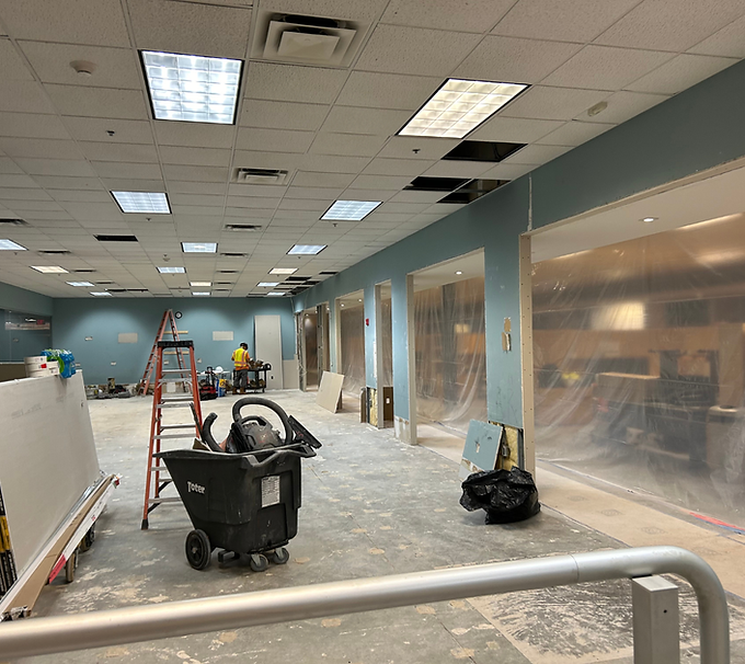 Construction zone inside an office space with drop ceilings, plastic-covered walls, and cleaning equipment.