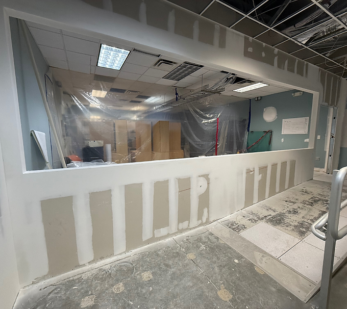Construction site with drywall, plastic-covered openings, and debris on the floor inside a building.