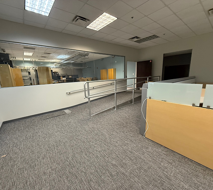 Empty office lobby with carpet, glass partitions, and a wheelchair-accessible ramp with handrails.