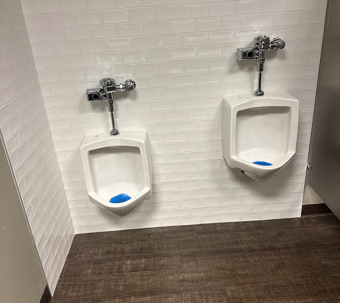 Two white urinals on a tiled restroom wall with a dark wood-look floor.