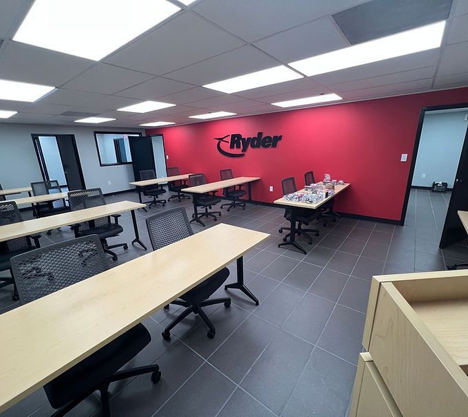 Empty office break room with tables, black chairs, a red Ryder logo wall, and tiled floor