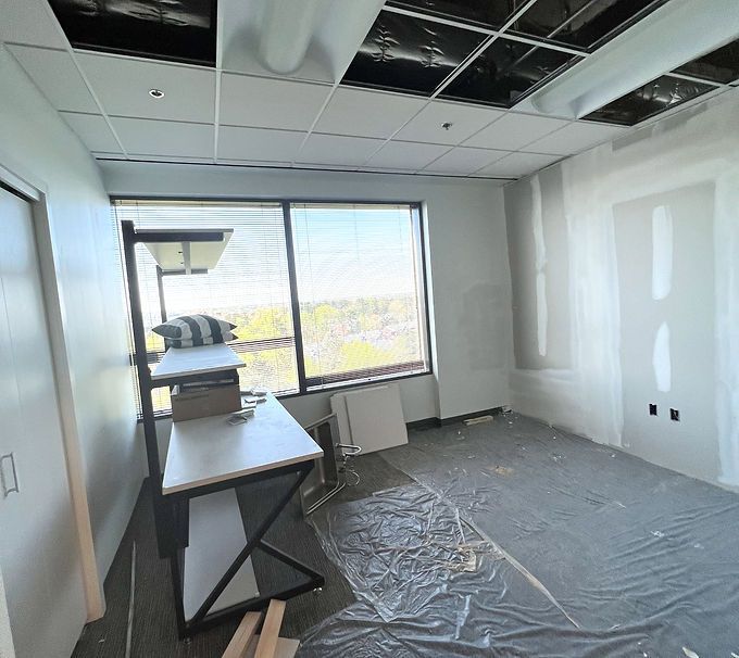 Partially renovated office with unfinished ceiling, covered floor, desk, and large window with city view