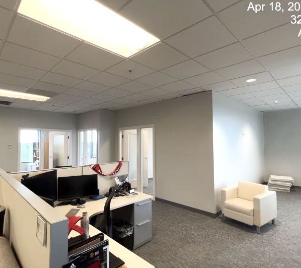 Empty office cubicles and a white lounge chair in a gray carpeted workspace.