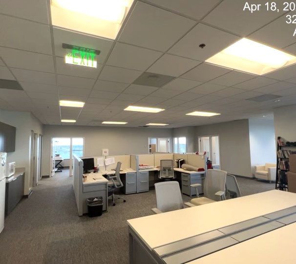 Empty office with gray cubicles, white desks, and fluorescent ceiling lights.