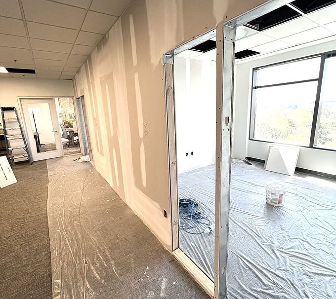 Renovated office hallway beside unfinished room with exposed ceiling and flooring work underway