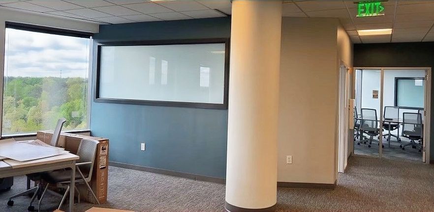 Modern office hallway with glass-walled conference room, white column, and chairs by large windows