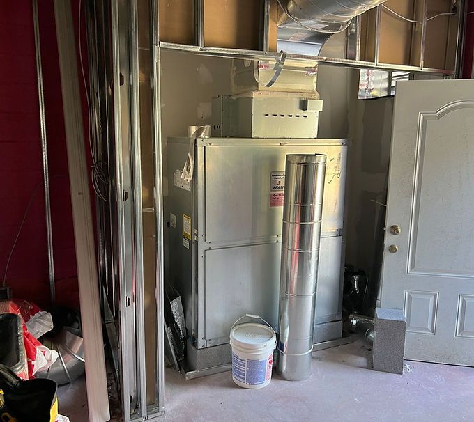 Partially finished room with exposed walls, furnace units, ductwork, and a white door beside a paint bucket.