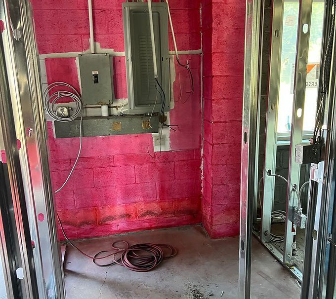 Empty room under construction with pink insulation, exposed electrical panels, and coiled wire on the floor