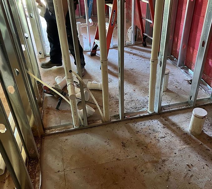 Partially framed room with exposed studs, pipes, and a concrete floor during construction