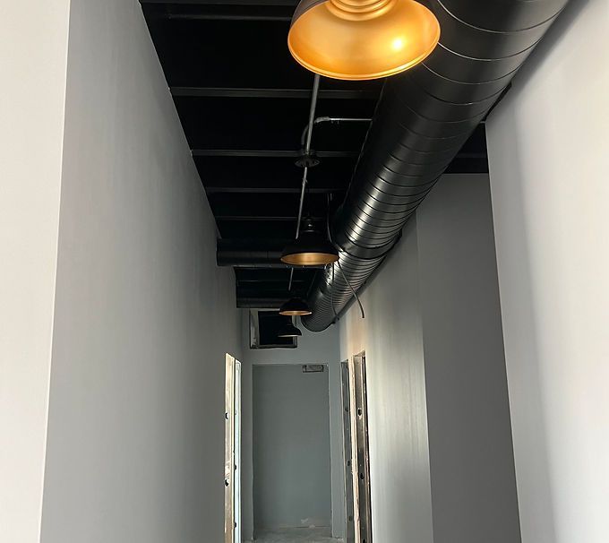 Narrow hallway with white walls, black ceiling, exposed ductwork, and hanging industrial lights