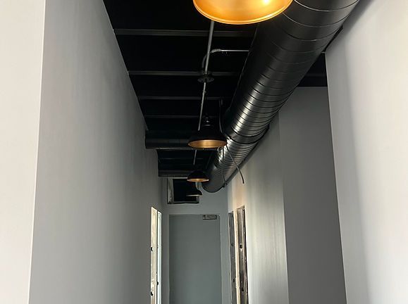Narrow hallway with white walls, black exposed ceiling, and warm hanging lights
