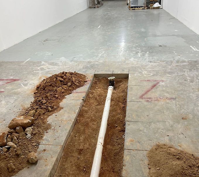 Floor trench with exposed white pipe in a concrete hallway under construction