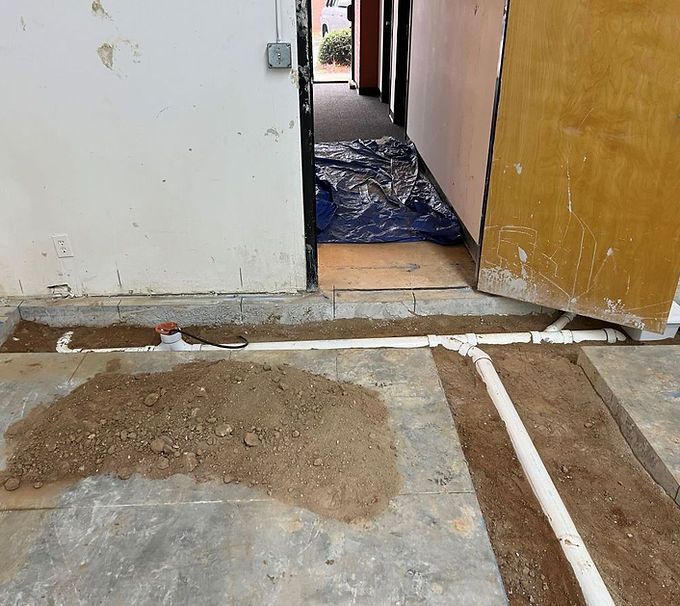 Damaged hallway floor with cracked concrete, exposed patchwork, and an open doorway covered with blue plastic.