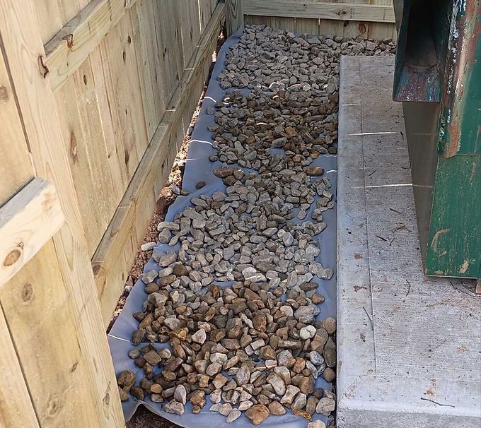 Gravel-filled drainage trench beside a wooden fence and concrete walkway