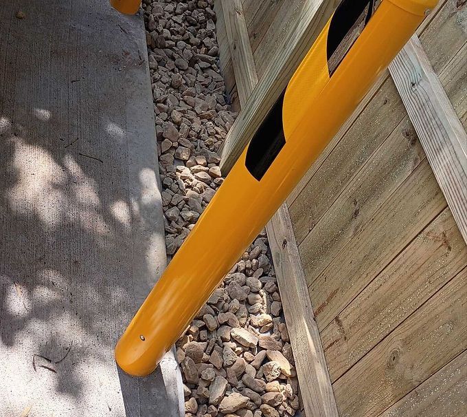 Yellow post in a narrow gravel path beside a wooden fence and concrete wall