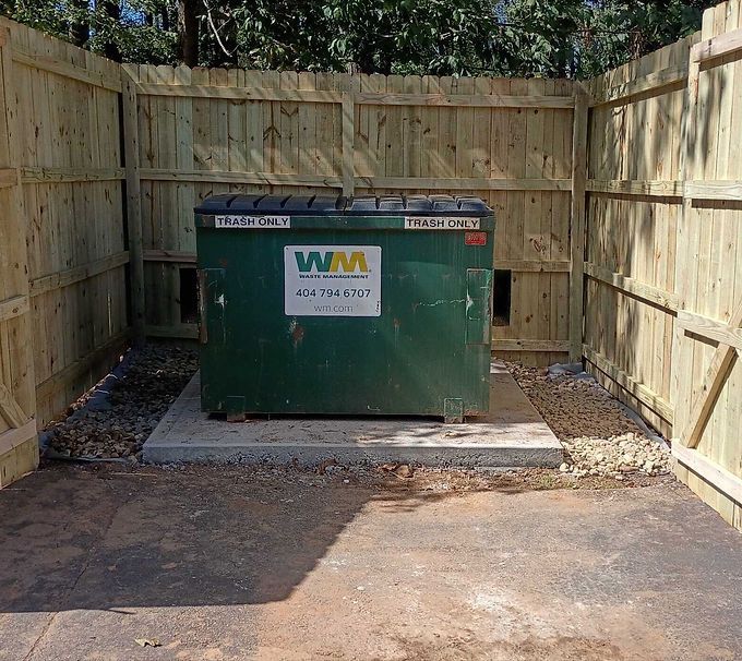 Green WM dumpster in a fenced concrete enclosure