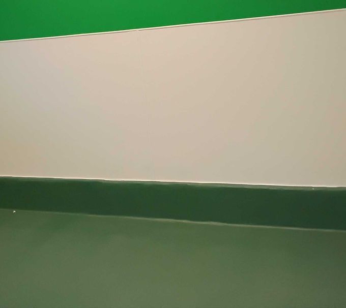 Empty beige wall above a green floor or ledge, with a thin horizontal seam