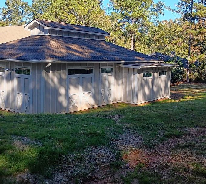 White shed with a dark roof and windows, sitting in a grassy yard with trees in the background