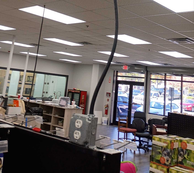 Empty office with desks, chairs, and bright ceiling lights; front windows show parked cars outside.