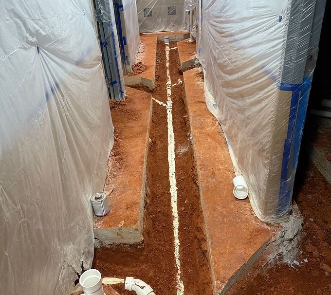 Narrow construction trench with red soil and plastic sheeting lining both sides