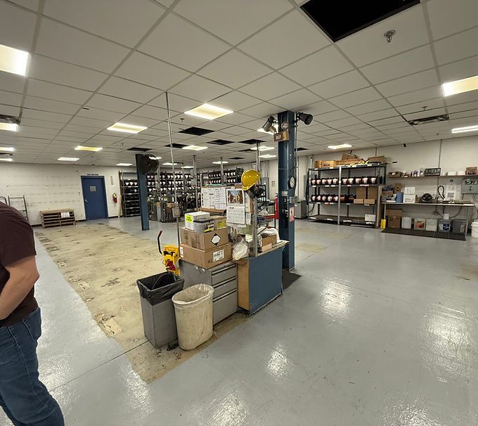 Spacious warehouse workroom with shelves, boxes, tables, and a partially visible person at left.