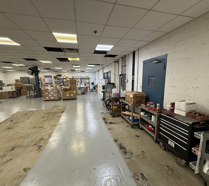 Warehouse aisle with boxes, tools, and metal shelving under fluorescent lights