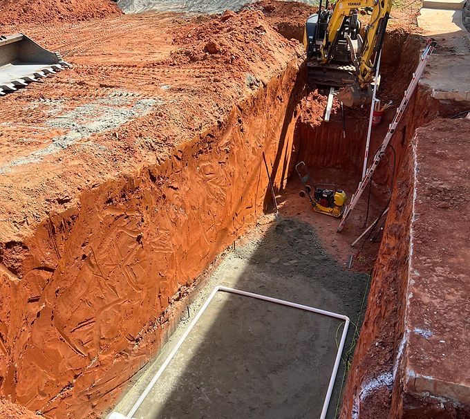 Excavator digging a deep red clay trench at a construction site