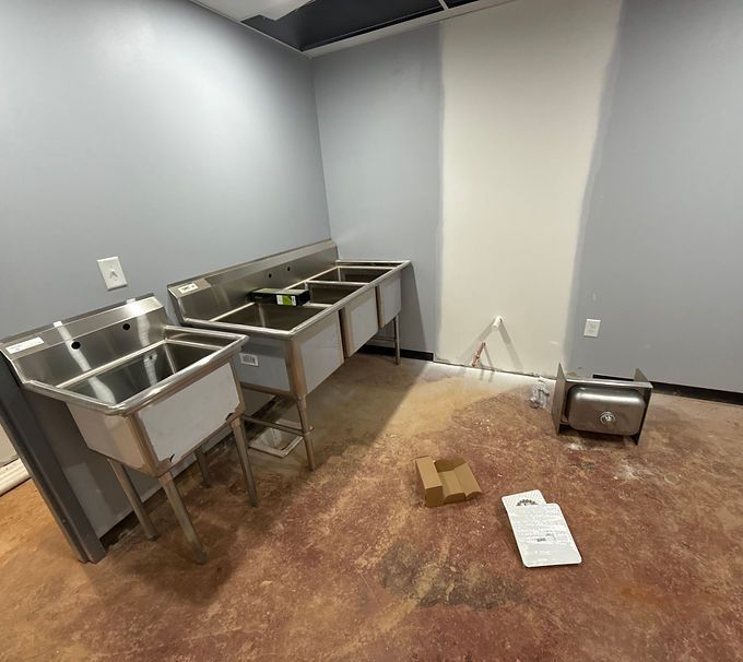 Empty kitchen room with stainless steel sinks, gray walls, and boxes on the floor