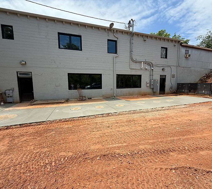 White industrial building with windows and doors beside a red dirt lot under a blue sky