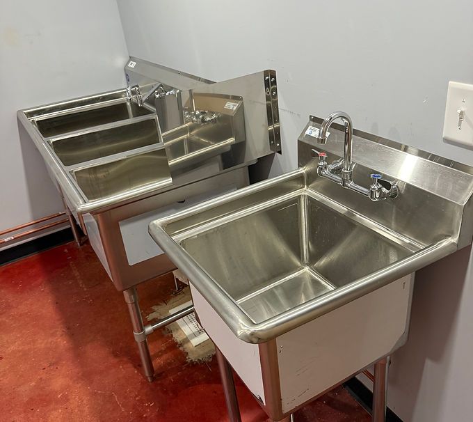 Two stainless steel wall-mounted sinks with faucets in a red-floored utility room