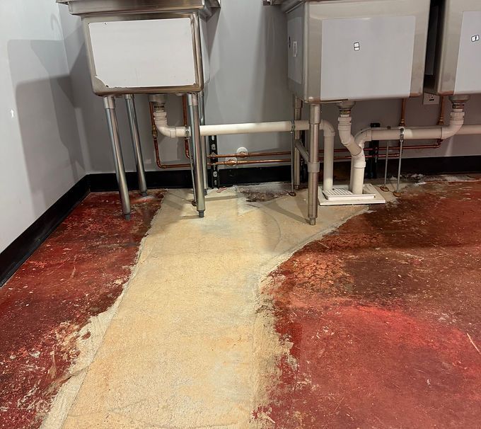 Restroom floor covered in red and cream spilled powder beneath white sinks and exposed pipes