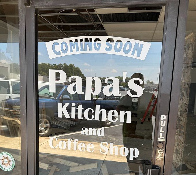 Storefront sign reading “Coming Soon Papa’s Kitchen and Coffee Shop” on a glass door.
