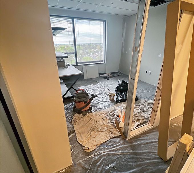 Office under renovation with plastic-covered floor, tools, and cardboard barriers near windows
