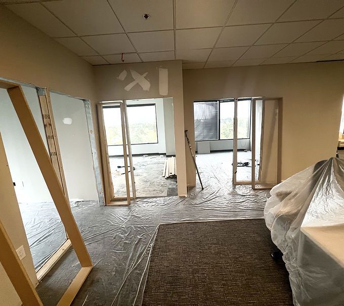 Renovated office with exposed framing, plastic-covered furniture, and carpeted floor under construction