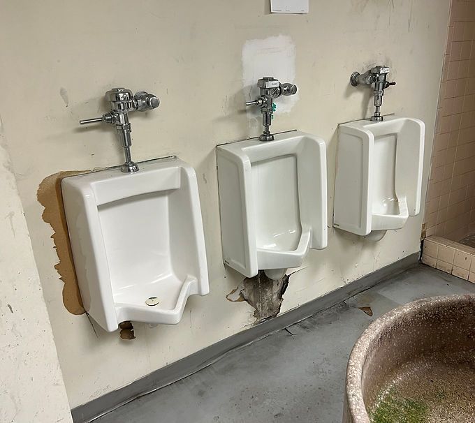 Three white urinals mounted on a bathroom wall beside a gray floor and sink edge.
