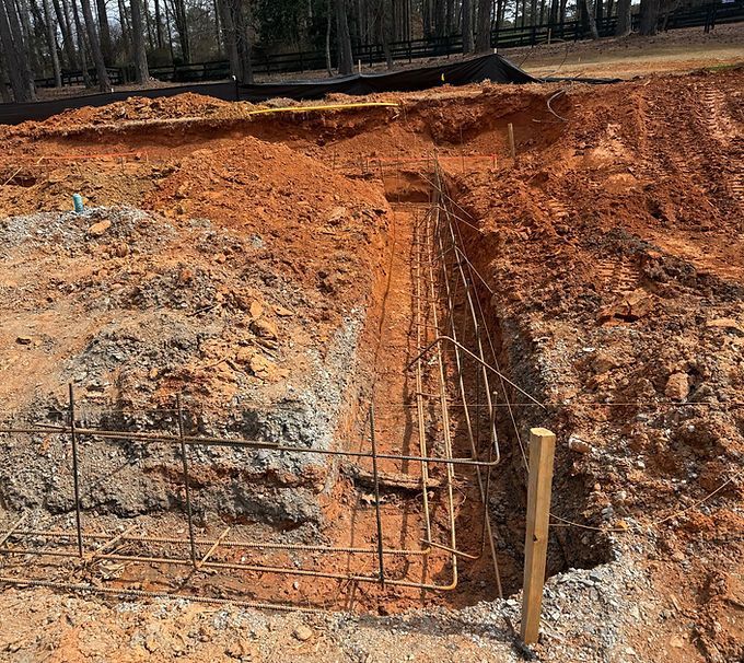Deep trench in red soil at a wooded construction site with exposed rebar foundation forms