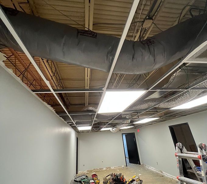 Partially finished room with exposed ceiling ducts, white walls, and construction debris on the floor