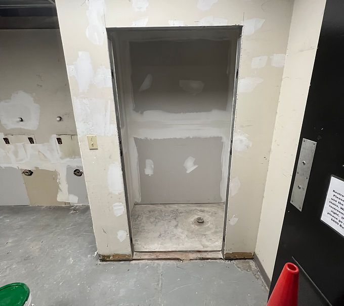 Small unfinished elevator alcove in a hallway with gray drywall, beige walls, and a concrete floor.