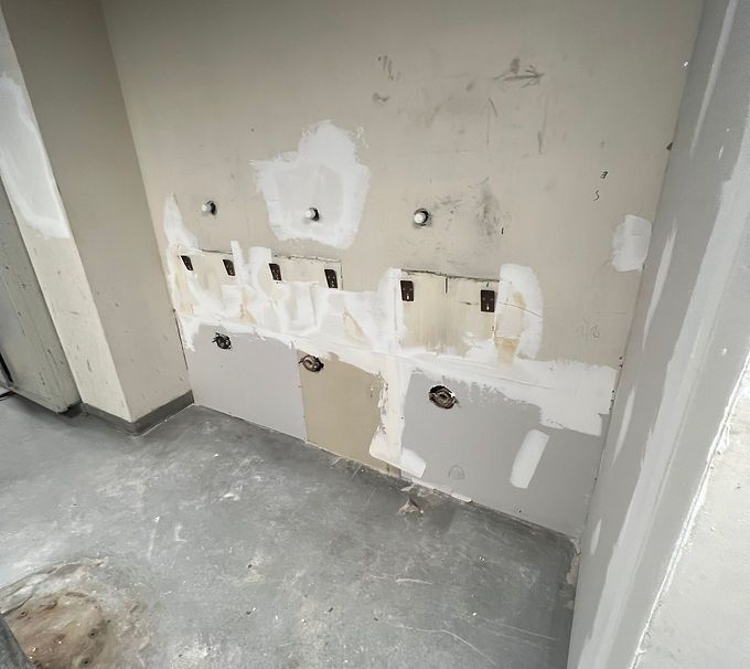 Partially repaired wall with patched drywall, holes, and exposed outlets in a bare room