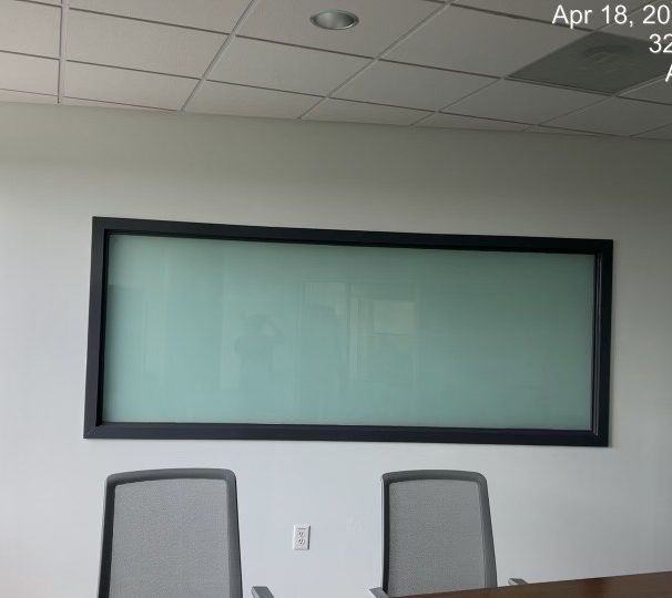 Conference room with a large wall-mounted display and two gray office chairs.