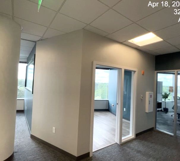 Empty office hallway with gray carpet, white walls, glass doorways, and a windowed room.